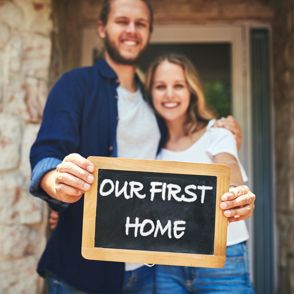 Couple holding up sign saying Our First Home